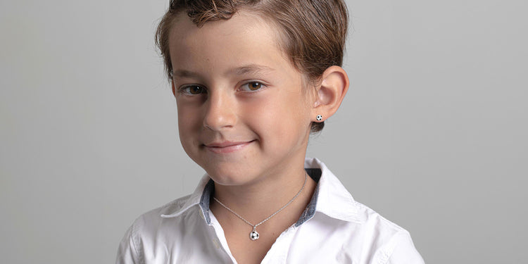 Lächelnder Junge trägt silberne Halskette mit Fußball-Anhänger und einen Fußball-Ohrstecker