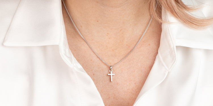 Silberne Halskette mit Kreuzanhänger am Dekolleté getragen