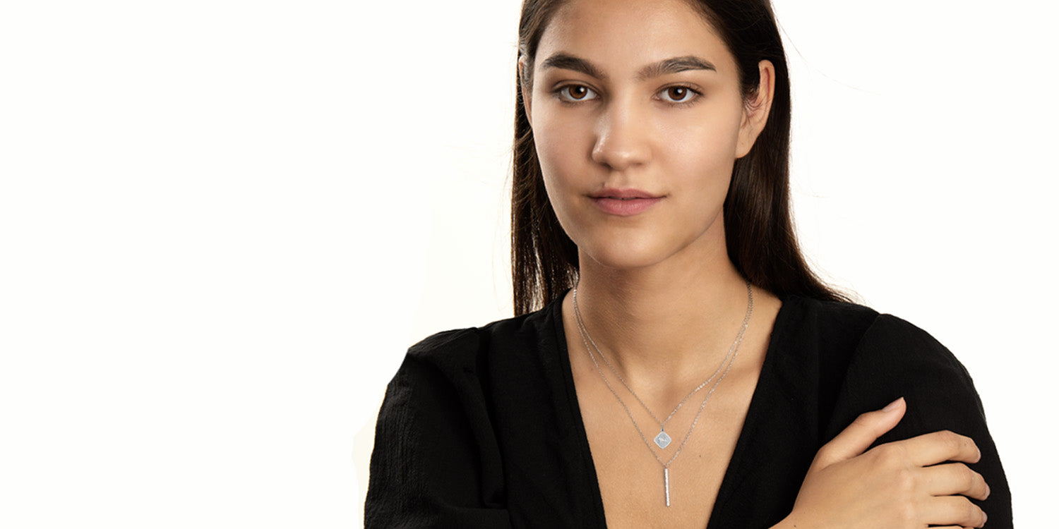 Frau in schwarzem Blazer trägt silberne Layering-Halsketten mit Sternzeichen-Anhänger und Stabanhänger