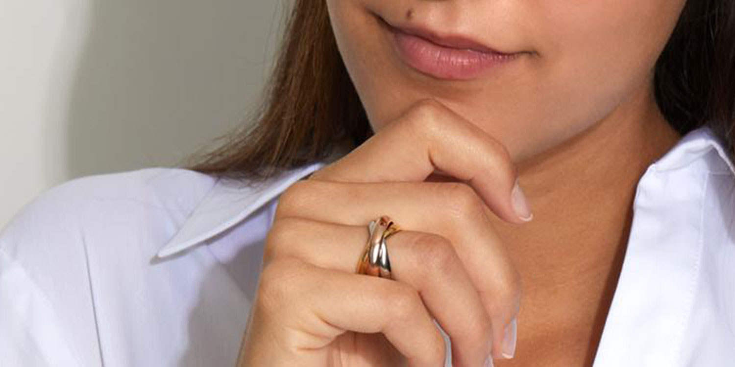 Frau in weißer Bluse trägt goldenen Ring mit drei ineinander verschlungenen Bändern