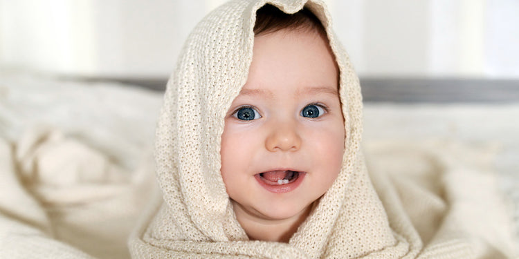 Lächelndes Baby mit blauen Augen in cremefarbenem Strickpullover mit Kapuze
