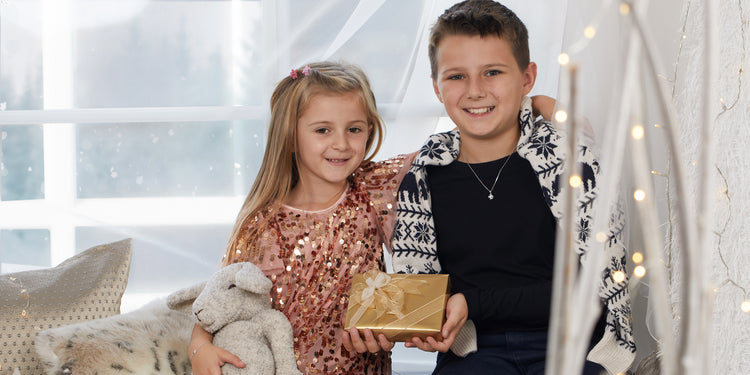 Lächelnde Geschwister mit goldener Geschenkbox - Mädchen in Paillettenkleid und Junge mit schwarzer Halskette