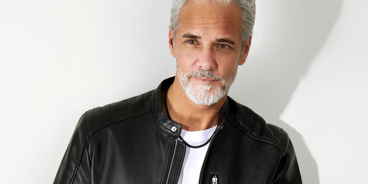 Mann mit grau-weißem Haar und Bart trägt schwarze Lederjacke und eine dunkle Halskette aus Leder - maskuliner Herrenschmuck